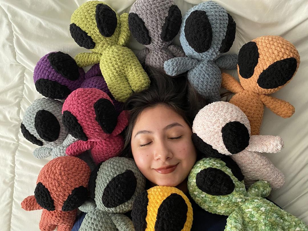 picture of monse, the owner of monse's crochet creations. She's surronded by plush aliens of various colors